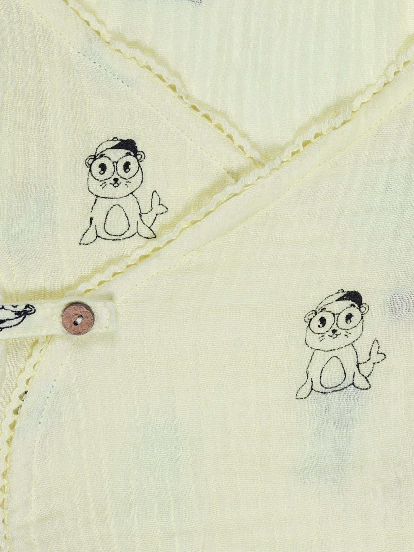 Close-up of wooden button and cartoon print on yellow organic cotton baby wrap shirt – breathable and eco-friendly fabric by Ray&Baby.