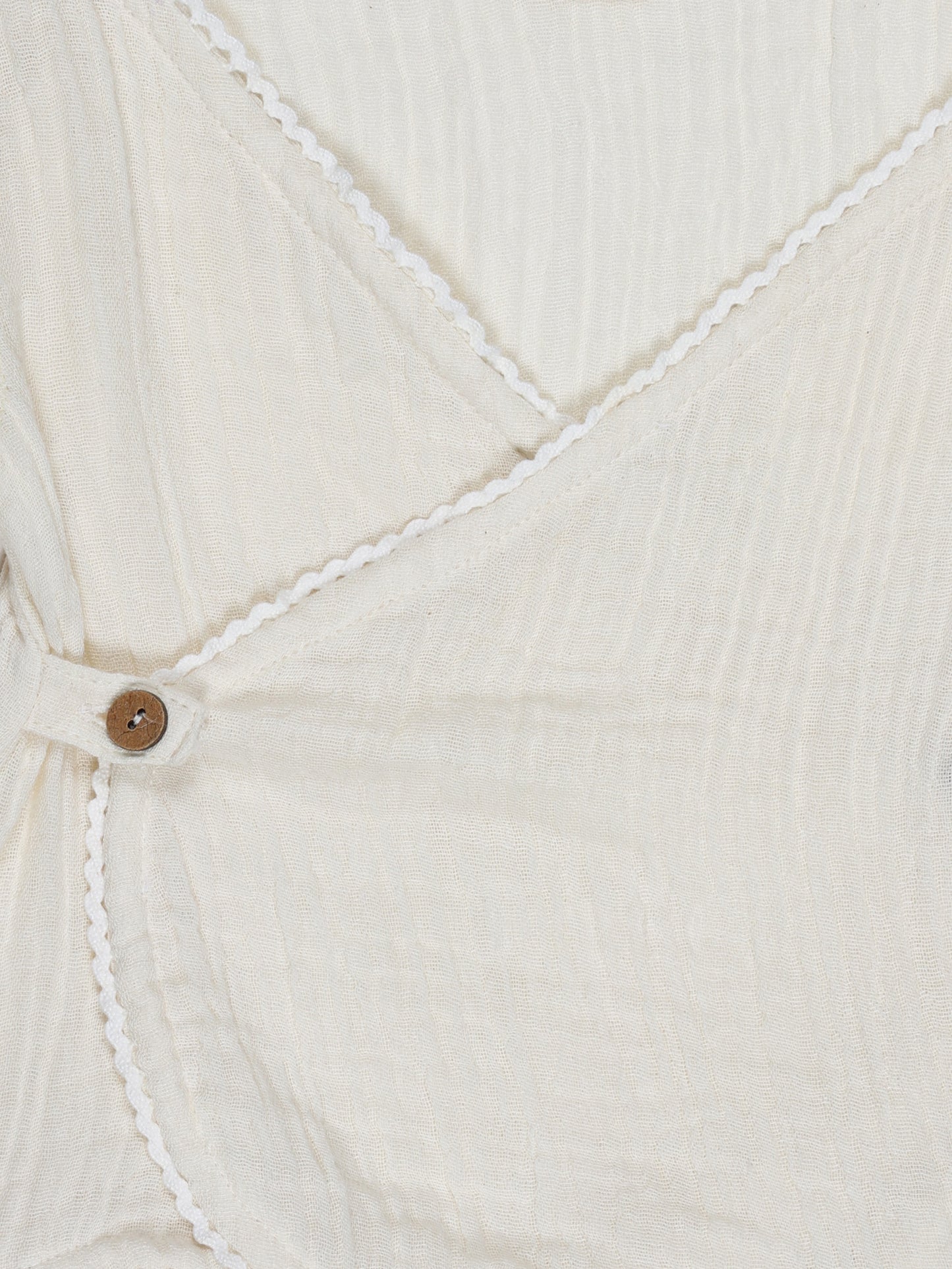 Close-up of lace lining and wooden button on neutral beige organic cotton baby shirt – soft and eco-friendly by Ray&Baby.